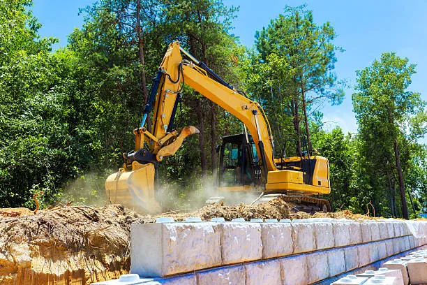 Excavator grading site alongside new retaining wall blocks