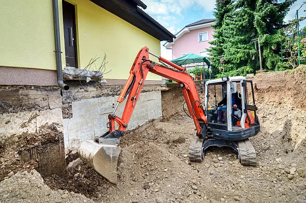 Mini excavator digging alongside residential foundation
