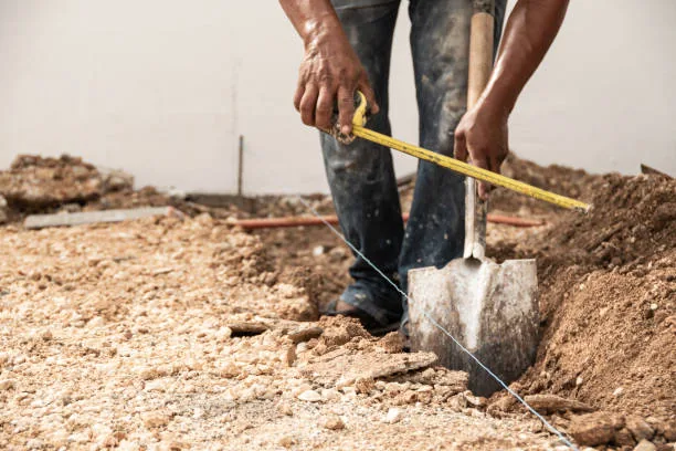 Worker measuring and digging trench for utility line