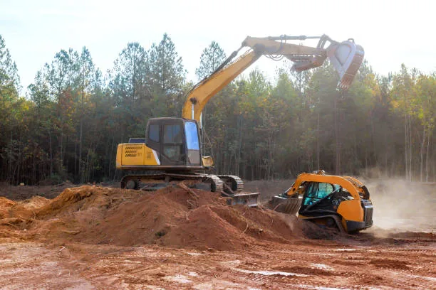 Excavator and skid steer clearing wooded land for development
